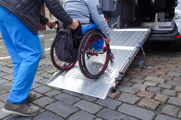 Assistant helping disabled person on wheelchair with transport using accessible van ramp